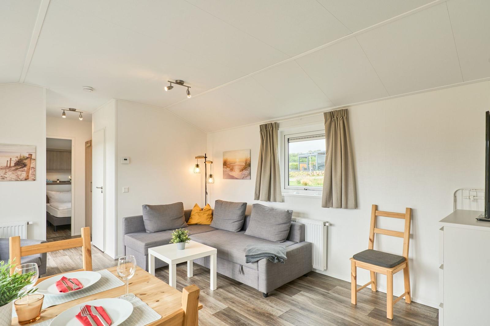 Wohn- und Essbereich mit Sofa, Tisch und Stühlen. Durchgang zur Schlafstube.