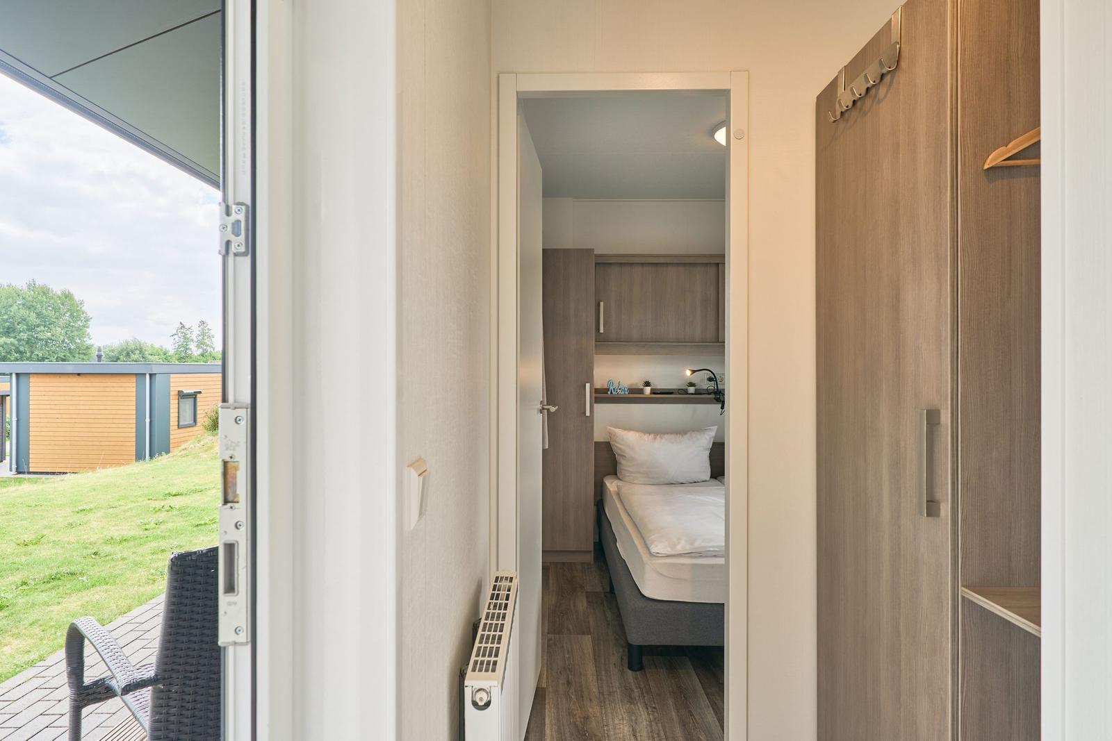 Schlafzimmer mit Bett und Kleiderschrank. Terrasse mit Sitzgelegenheit und Blick auf Grünfläche.