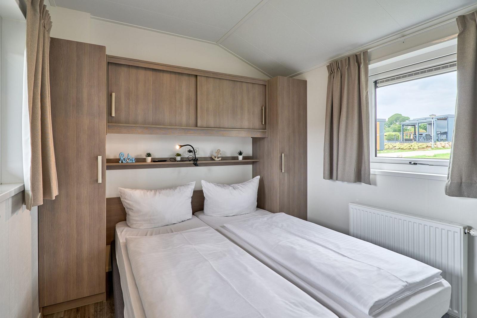 Zwei Betten mit weißen Bettwäschen, Holzschränke und Fenster mit Blick nach draußen.