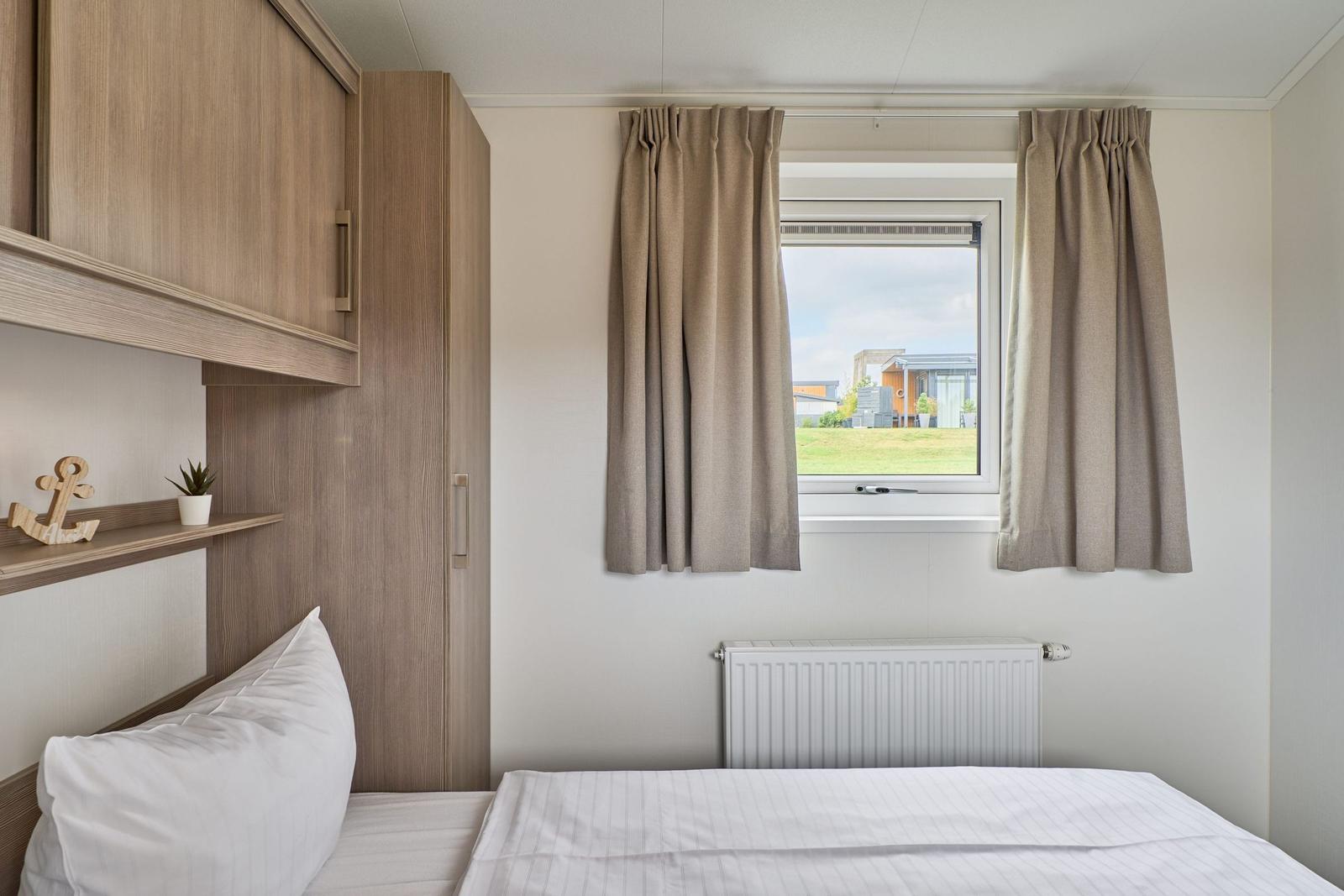 Schlafzimmer mit Bett, Schrank und Fenster mit Blick auf Grünfläche.