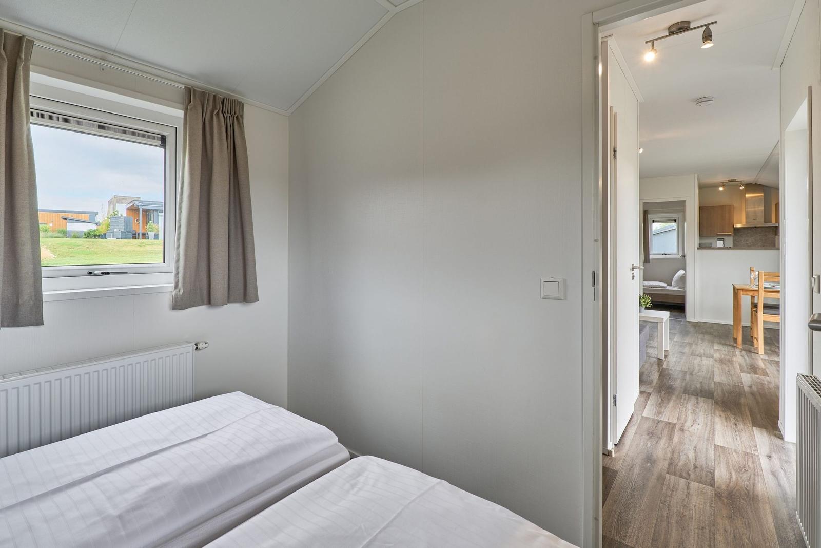 Zimmer mit Doppelbett und Fenster. Blick in die Küche und Wohnbereich.