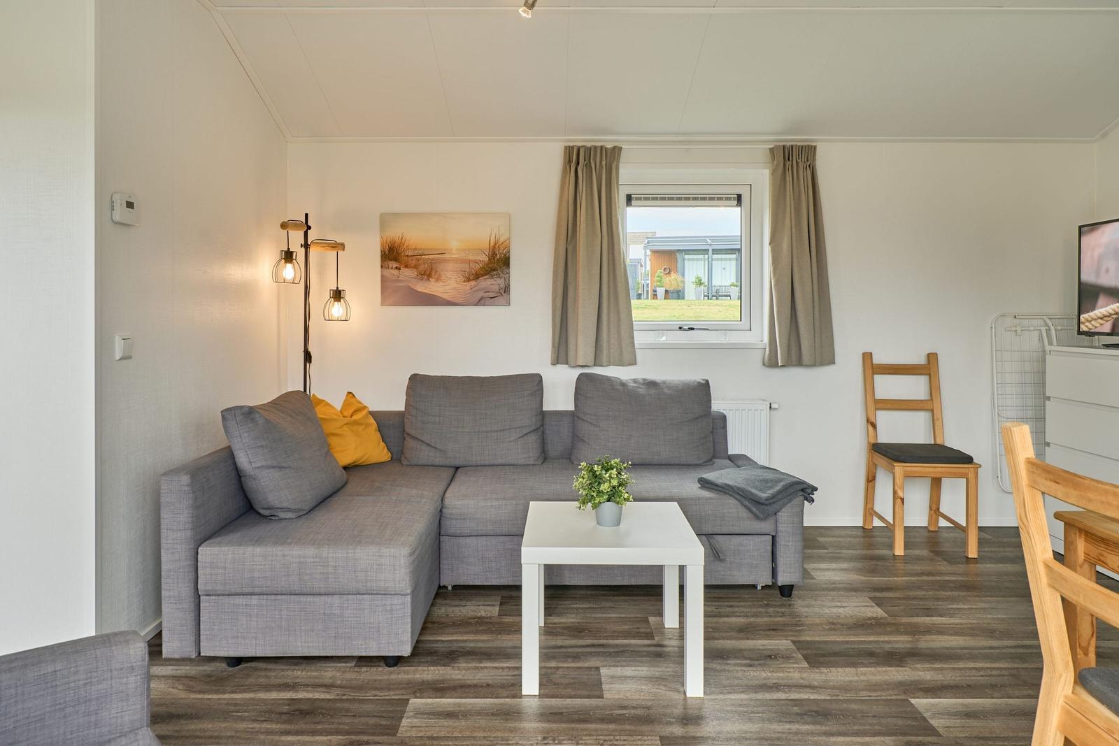 Wohnzimmer mit grauem Sofa, Tisch und Fenster.