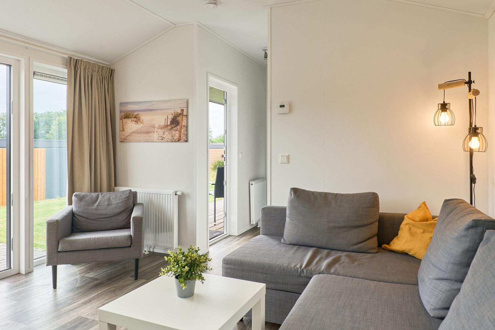 Wohnzimmer mit Sofa, Sessel und Tisch. Durchgang zu Terrasse und Garten.