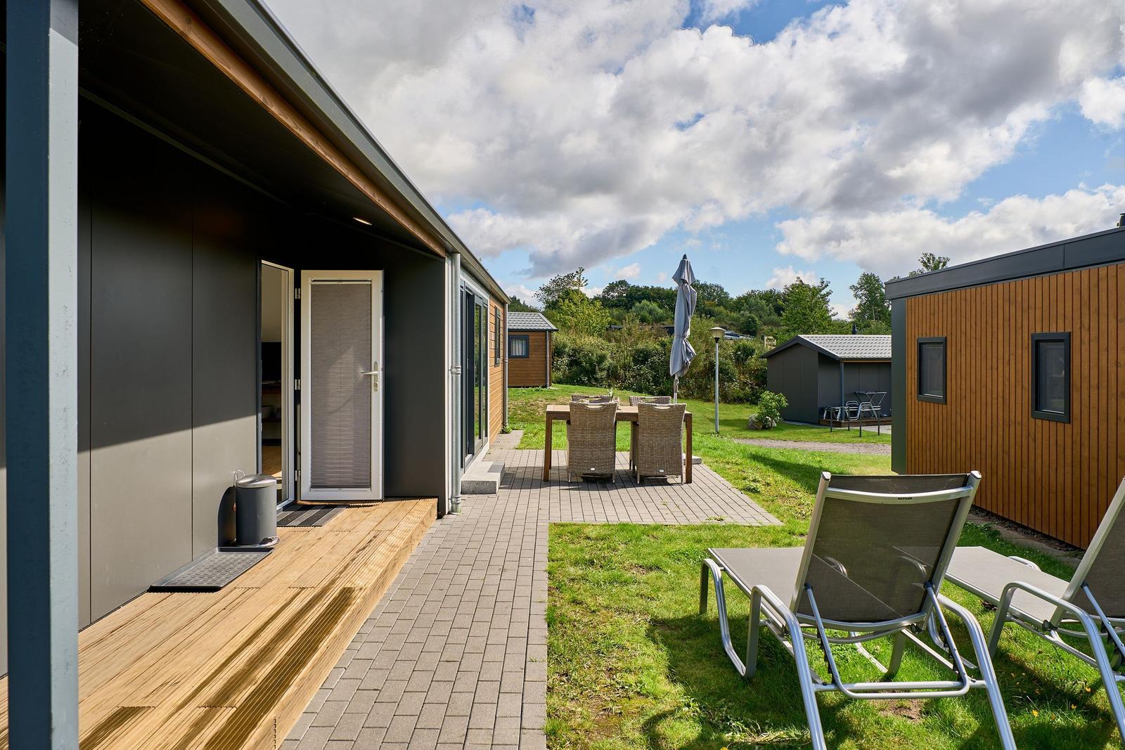 Terrasse mit Liegestühlen und Tisch. Hinterhof mit Gras und weiteren Häusern.