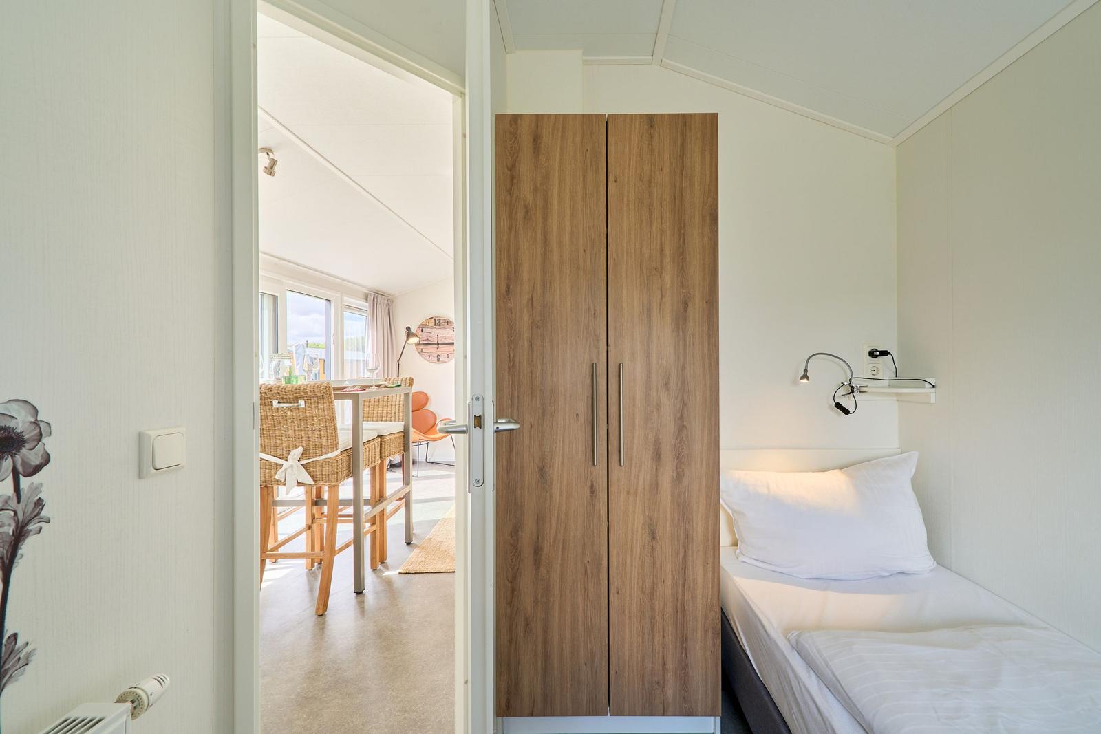 Schlafzimmer mit Bett, Kleiderschrank und Blick in Essbereich.