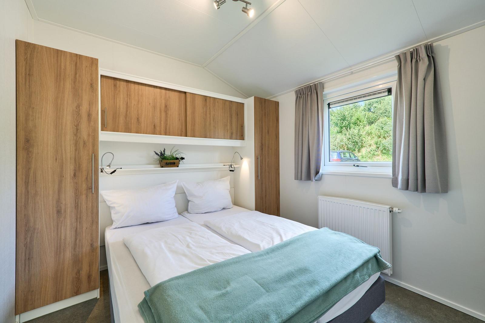 Schlafzimmer mit Doppelbett, Holzschränken und Fenster mit Blick auf Grün.