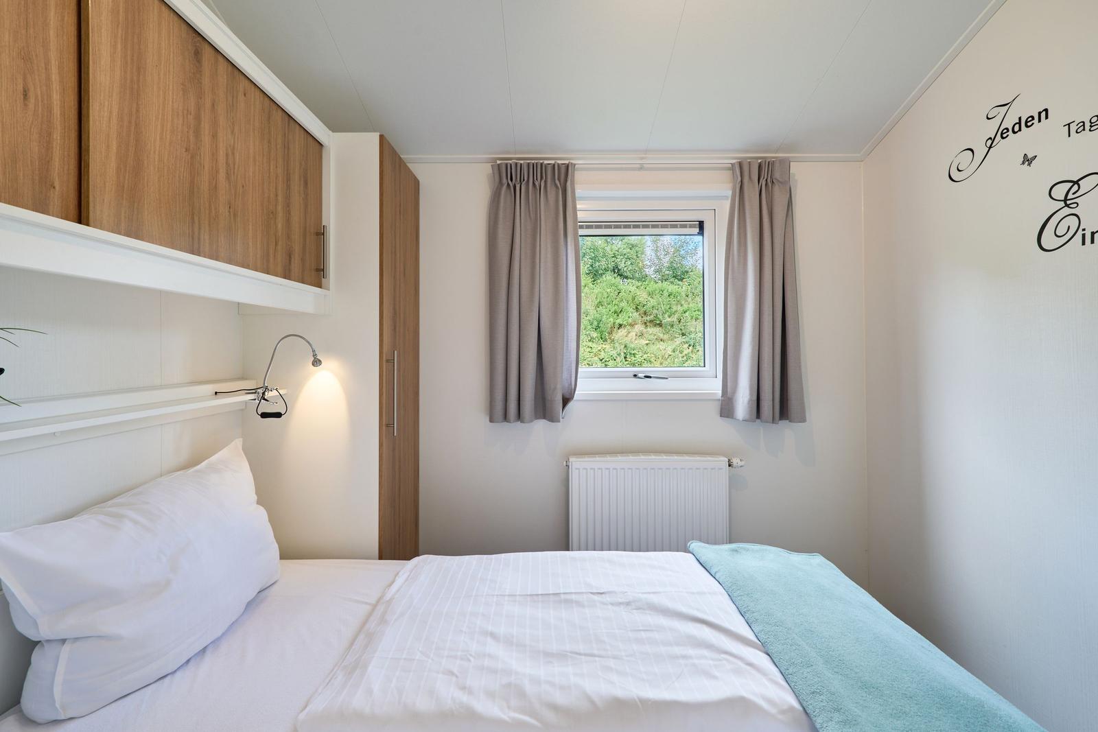 Schlafzimmer mit Bett, Fenster und Holzschränken.
