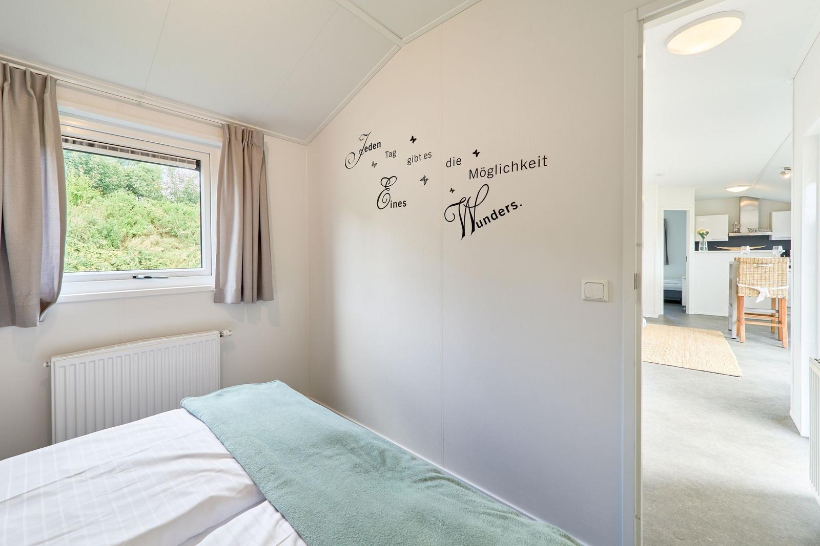 Schlafzimmer mit Bett, Fenster und Wanddekoration. Blick in die Küche.