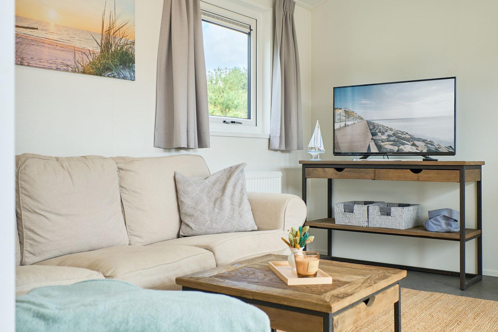 Wohnzimmer mit Sofa, Fernseher und Fenster. Auf dem Tisch steht eine Kerze.