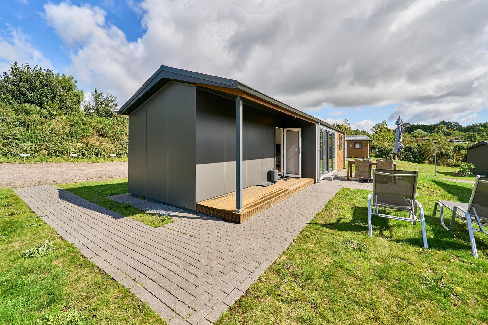 Moderne Hütte mit Terrasse und Gartenmöbeln. Grün umgeben mit Blick auf Wald.