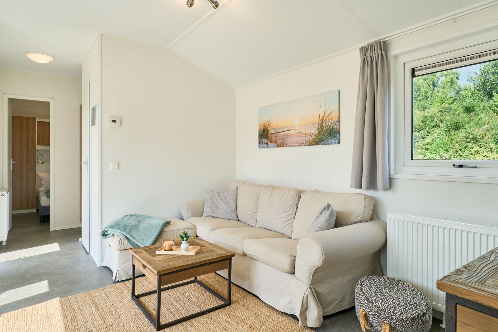 Wohnzimmer mit Sofa, Couchtisch und Fensterblick auf Grün.