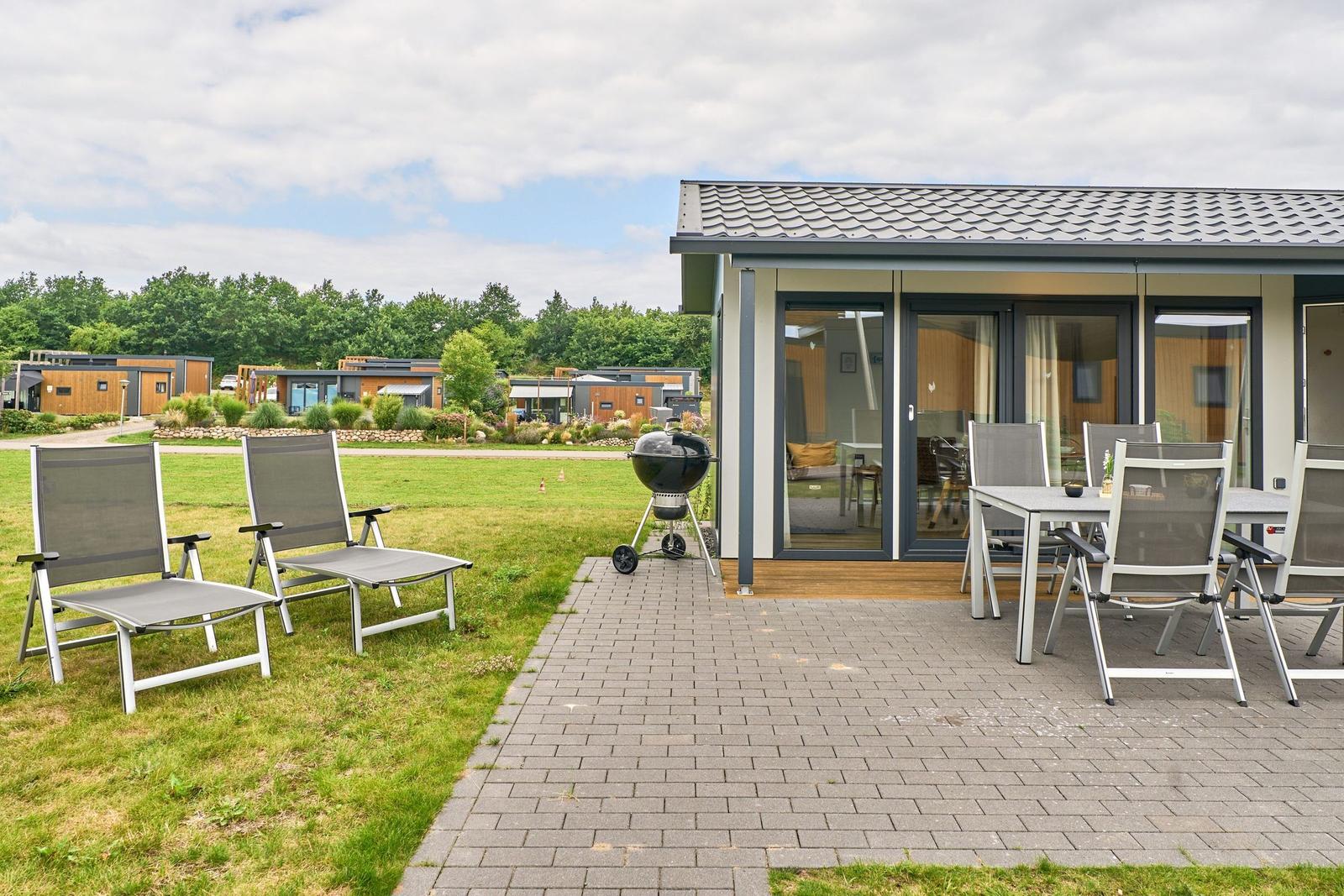 Terrasse mit Grill, Tisch und Stühlen. Hintergrund: Grasfläche und Ferienhäuser.