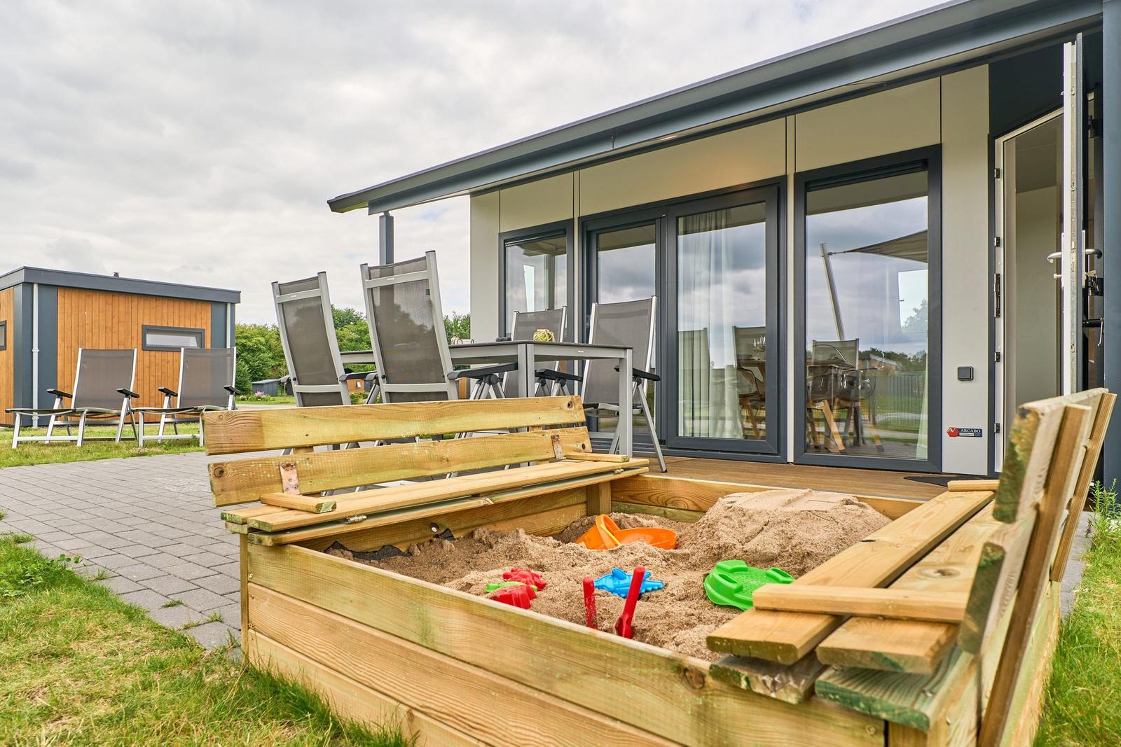 Außenbereich mit Sandkasten, Gartenmöbeln und Terrasse vor modernem Haus.