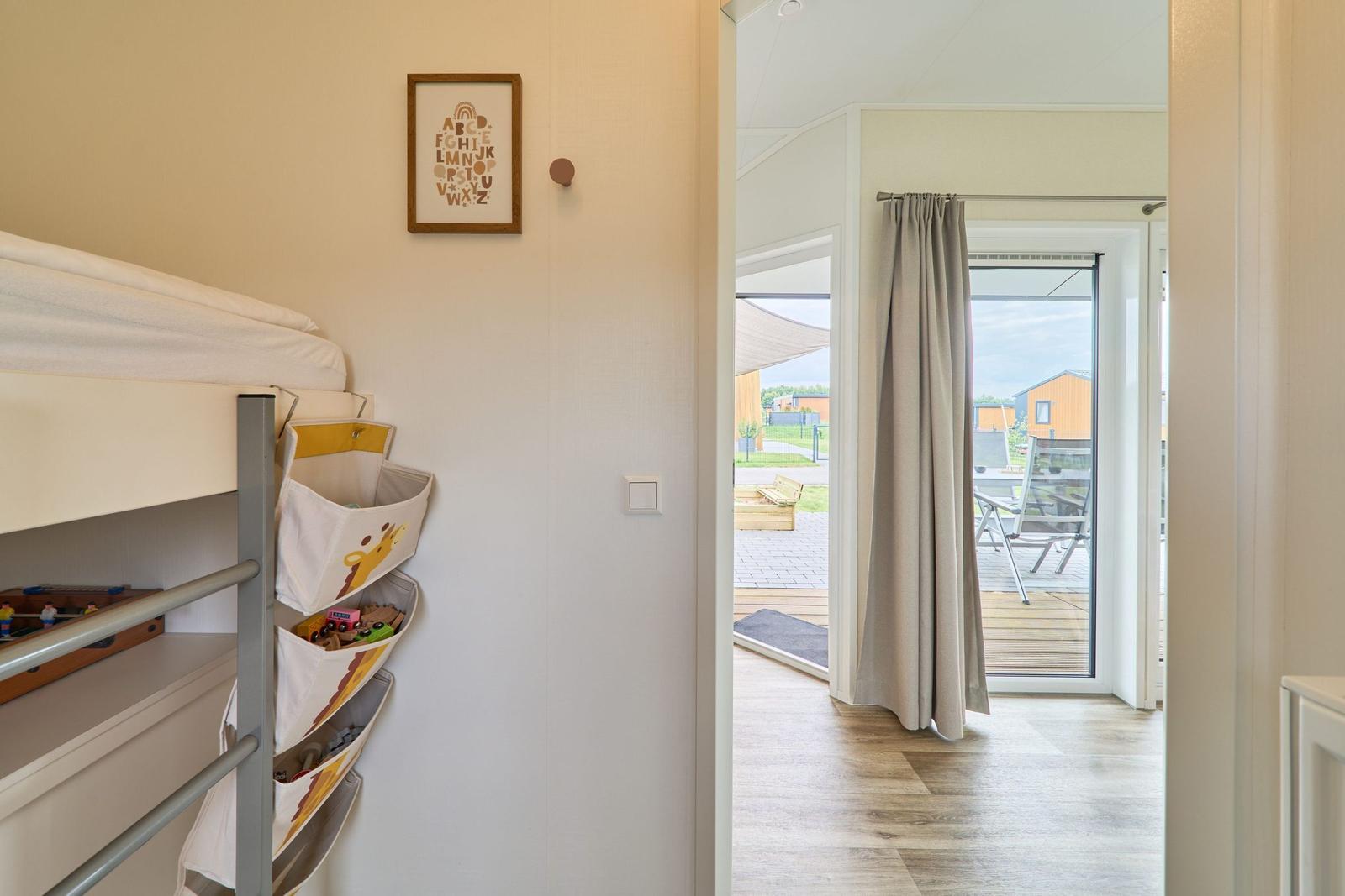 Kinderzimmer mit Doppelstockbett und Spielzeugregal. Durchgang zur Terrasse mit Blick auf Garten.