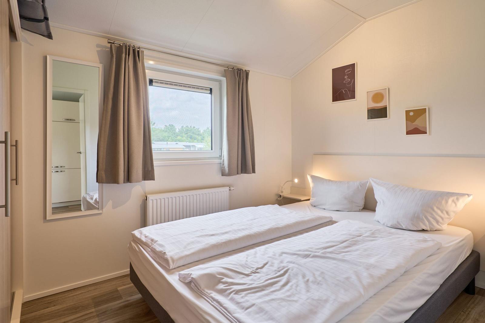 Schlafzimmer mit Doppelbett, Fenster und Wandbildern.