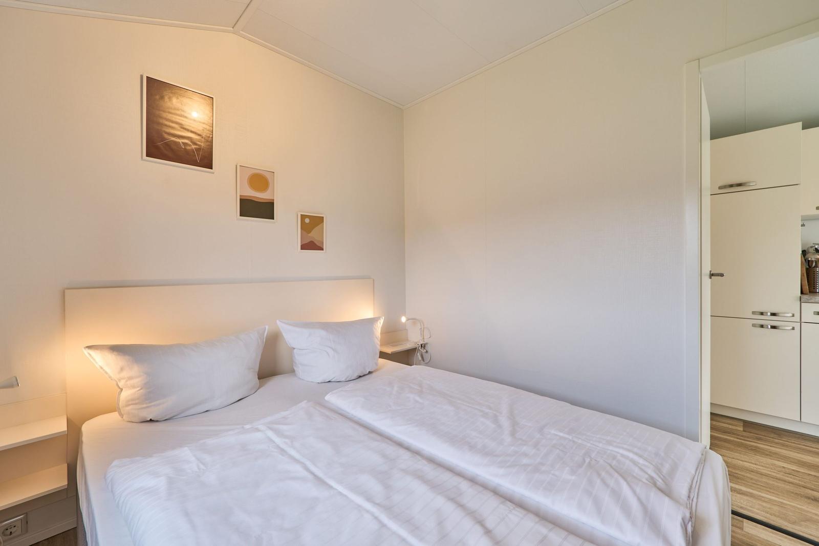Schlafzimmer mit Doppelbett, Wandbildern und angrenzender Küche.