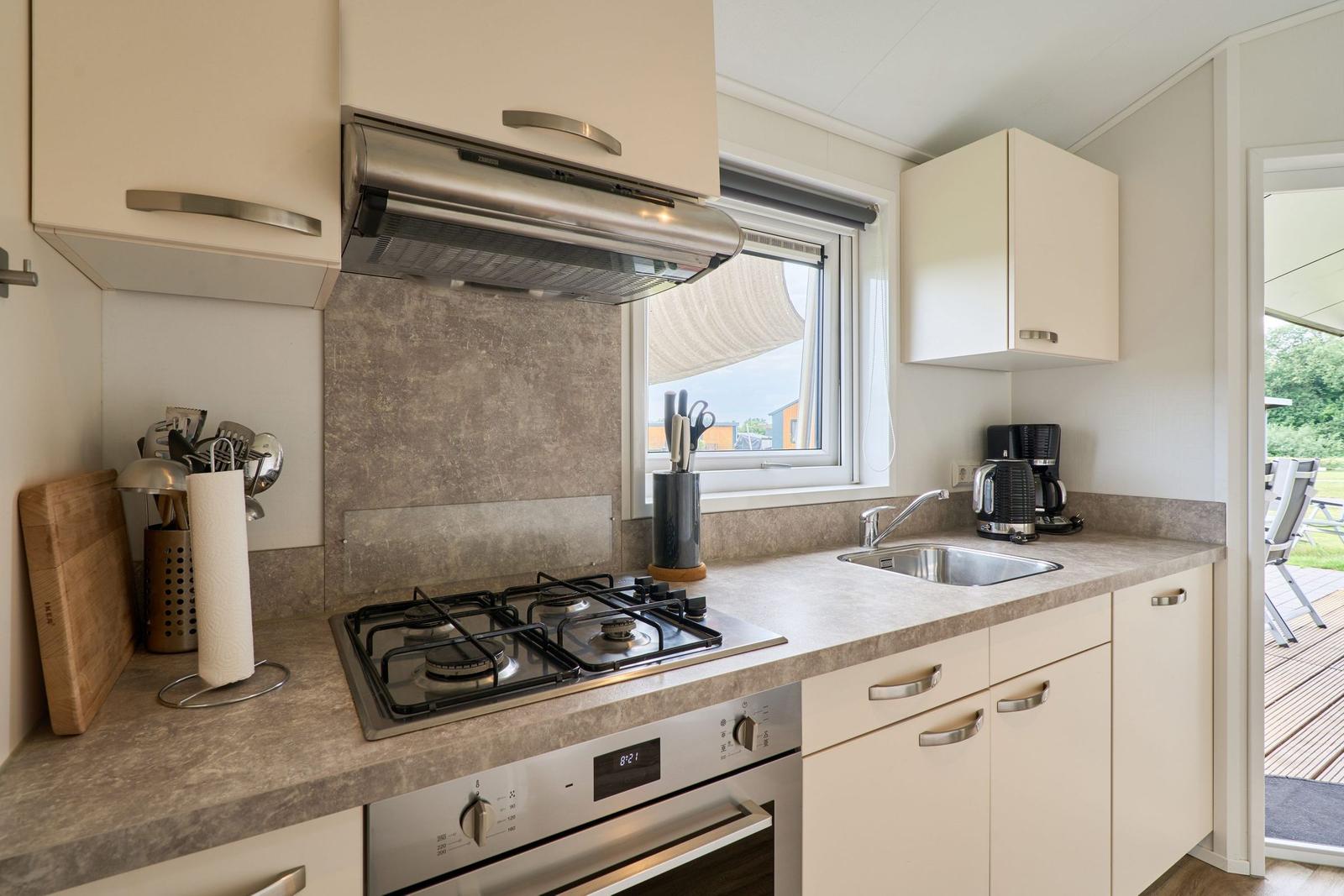 Küche mit Herd, Spüle und Fenster. Außenterrasse sichtbar.