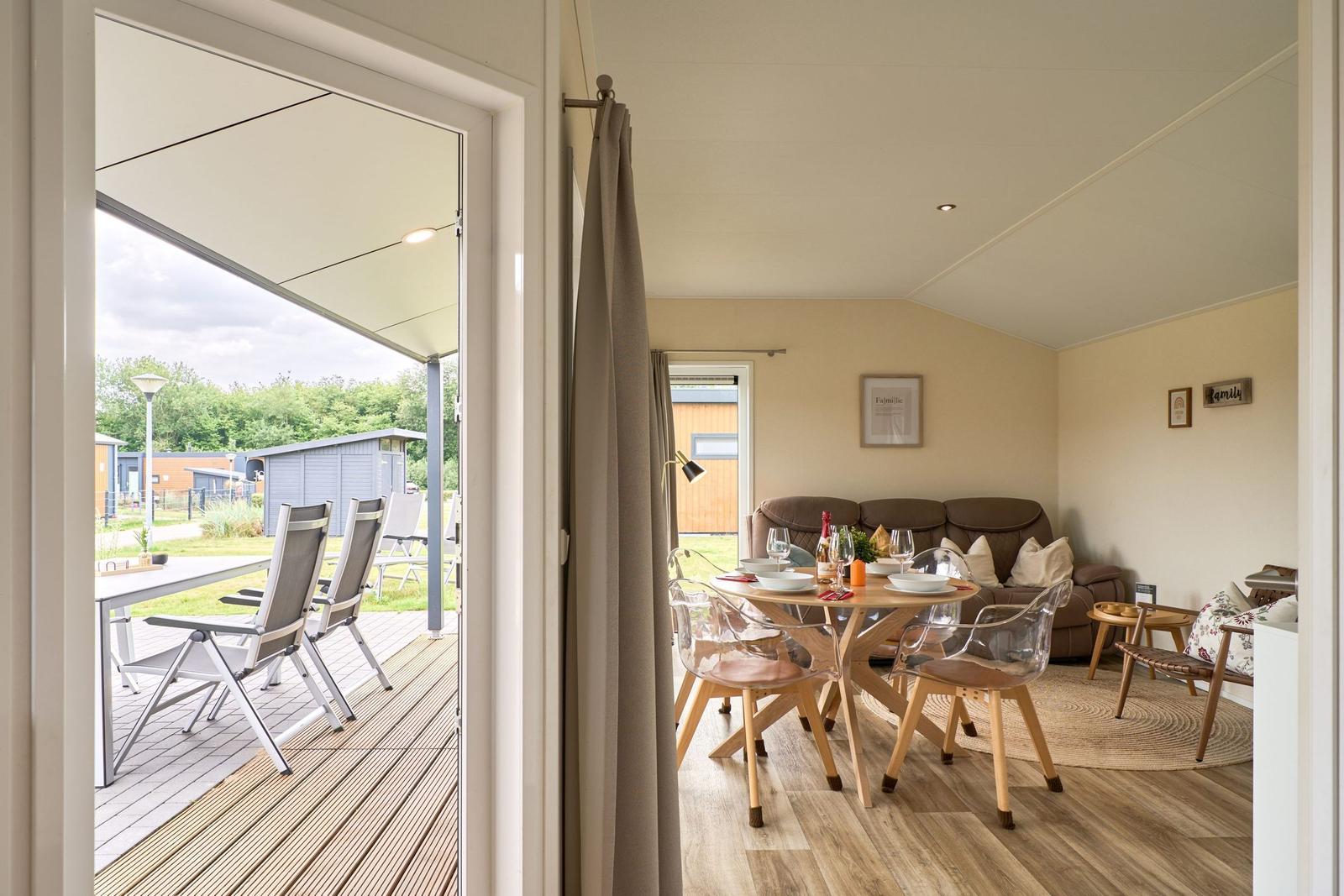 Ein Essbereich mit Tisch und Stühlen. Durch eine Tür ist eine Terrasse mit Stühlen sichtbar.