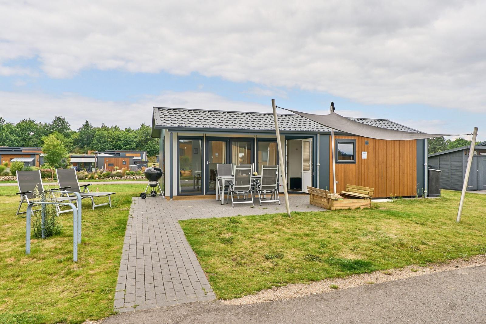 Moderne Ferienhaus mit Terrasse, Grill und Sitzgelegenheiten im Freien.