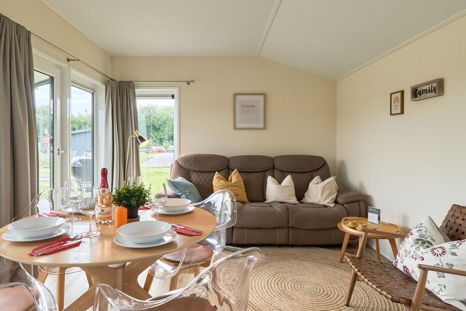 Wohn- und Essbereich mit Sofa, Tisch und Stühlen. Fenster mit Blick nach draußen.
