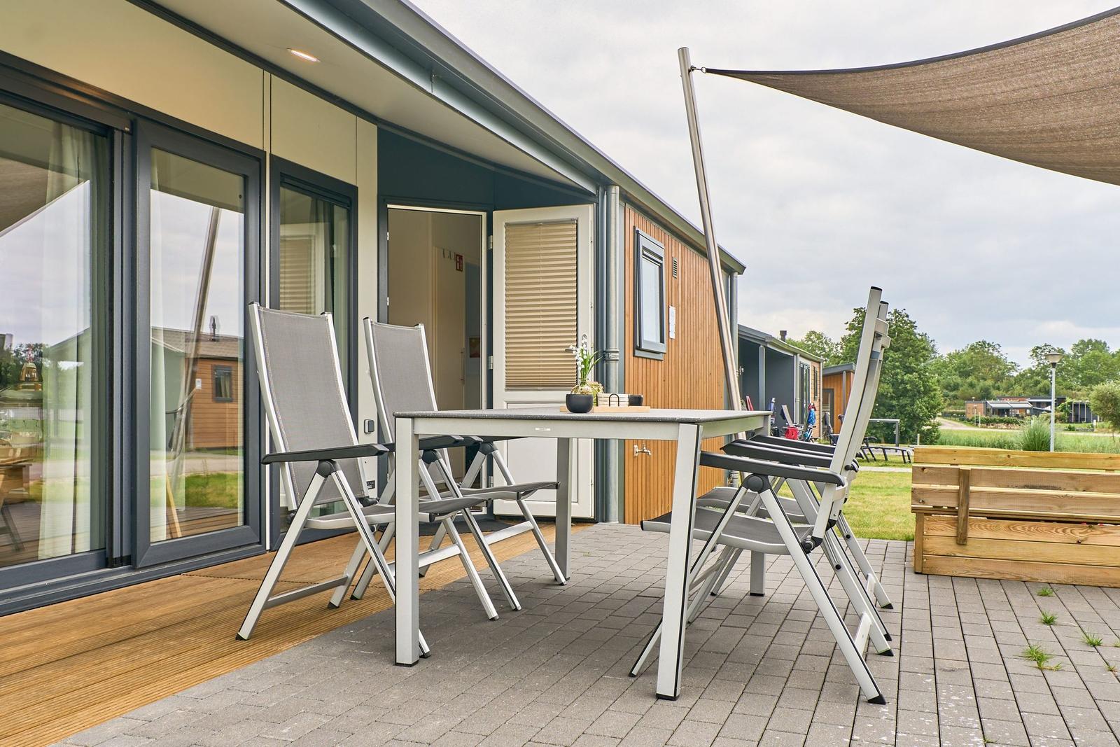 Terrasse mit Tisch, Stühlen und Sonnensegel. Holz- und Steinbelag.