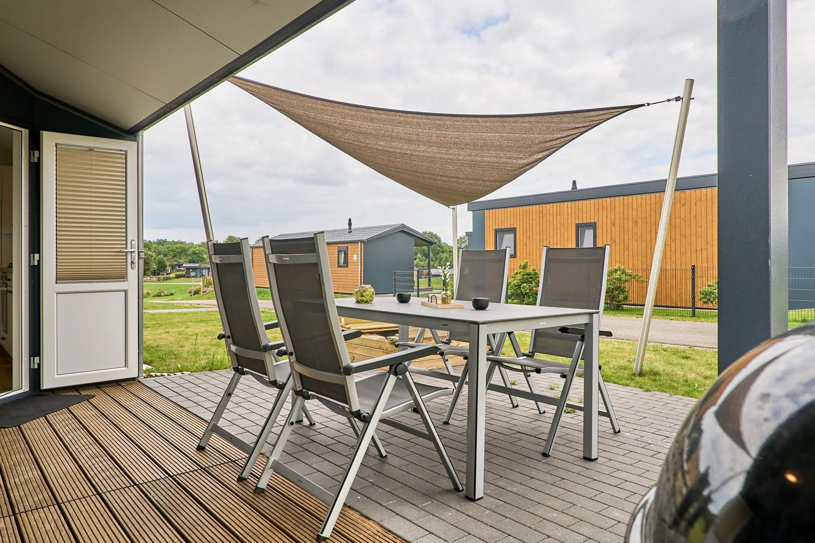 Terrasse mit Tisch, Stühlen und Sonnensegel. Hintergrund: Wohnmobile und Grünflächen.