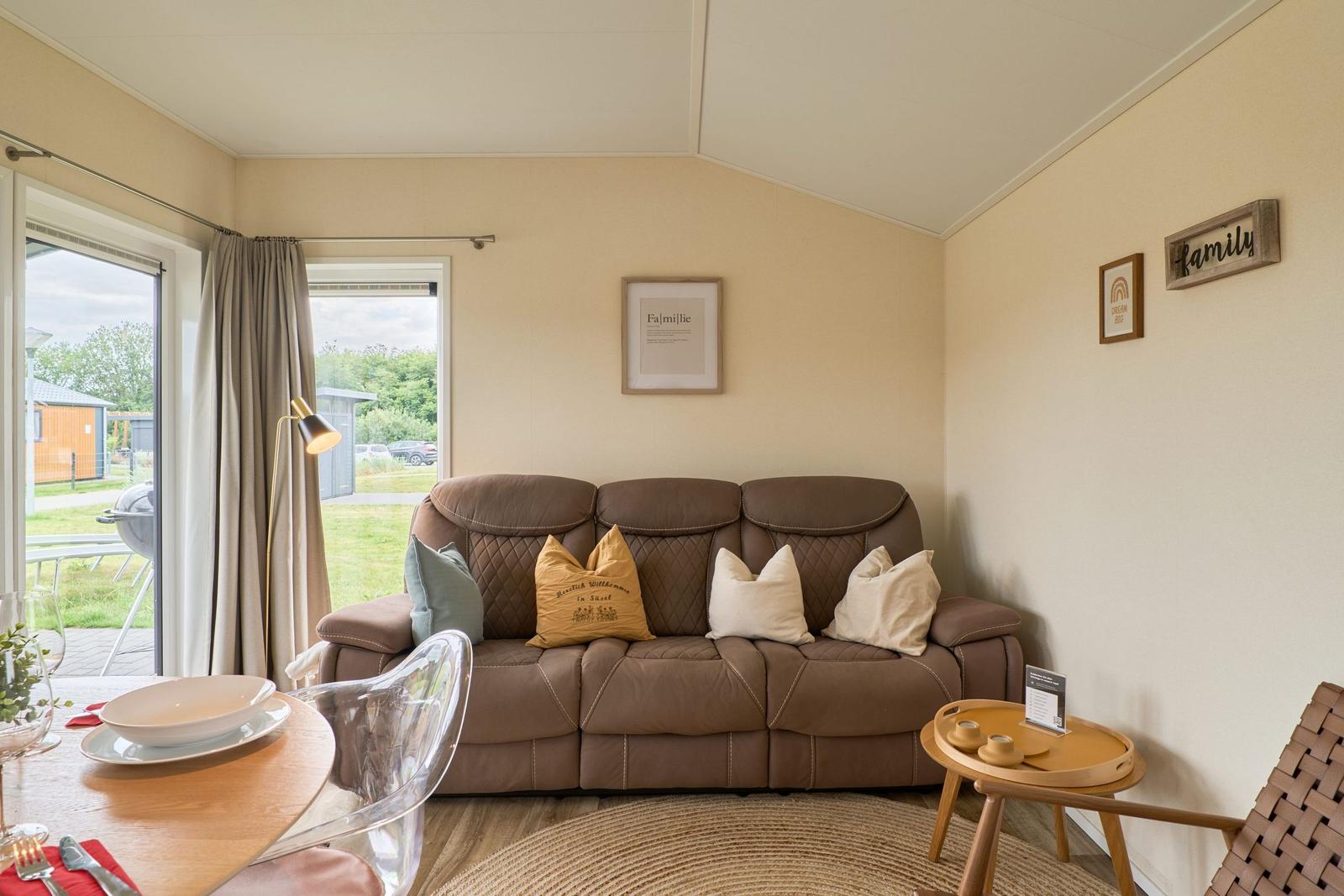 Ein Wohnzimmer mit braunem Sofa, Tisch und Fenster zur Außenseite.