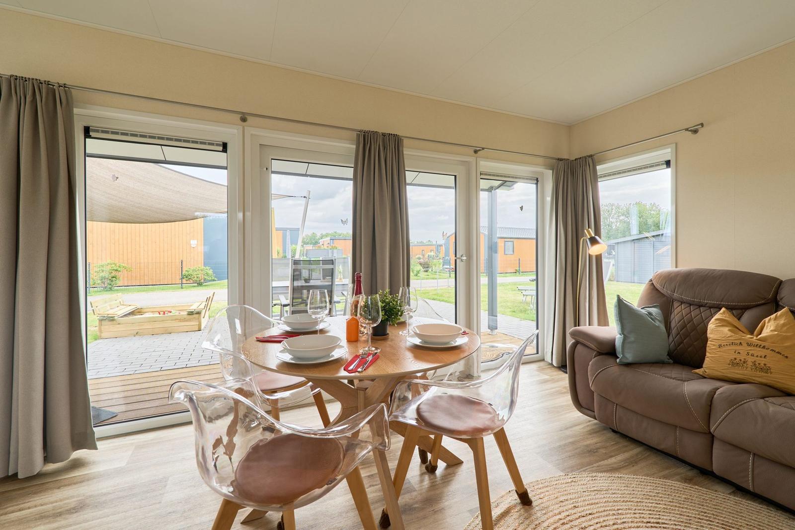 Essbereich mit Tisch und transparenten Stühlen. Sofa mit Kissen. Blick auf Terrasse und Garten.