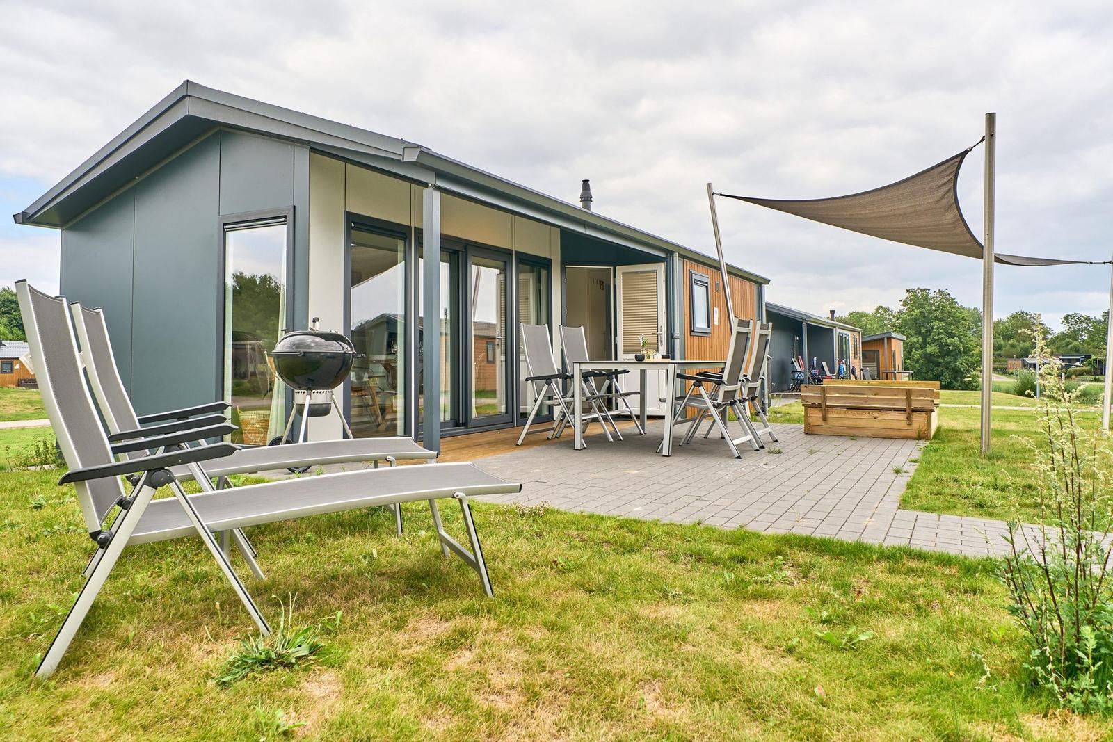 Modernes Ferienhaus mit Terrasse, Grill und Sitzgelegenheiten im Freien.