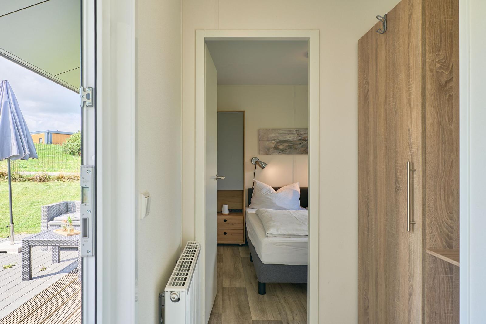 Schlafzimmer mit Bett, Nachttisch und Kleiderschrank. Durchgang zur Terrasse mit Gartenblick.