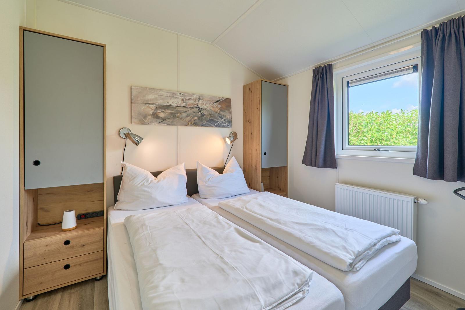 Zwei Einzelbetten mit weißen Bettwäschen, Wandspiegel und Fenster mit Blick auf Grün.