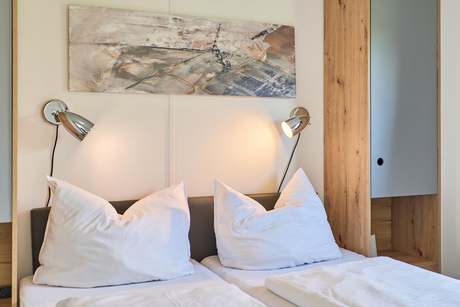 Zwei Betten mit weißen Kissen und Bettwäsche unter einer Wanddekoration mit zwei Wandlampen.