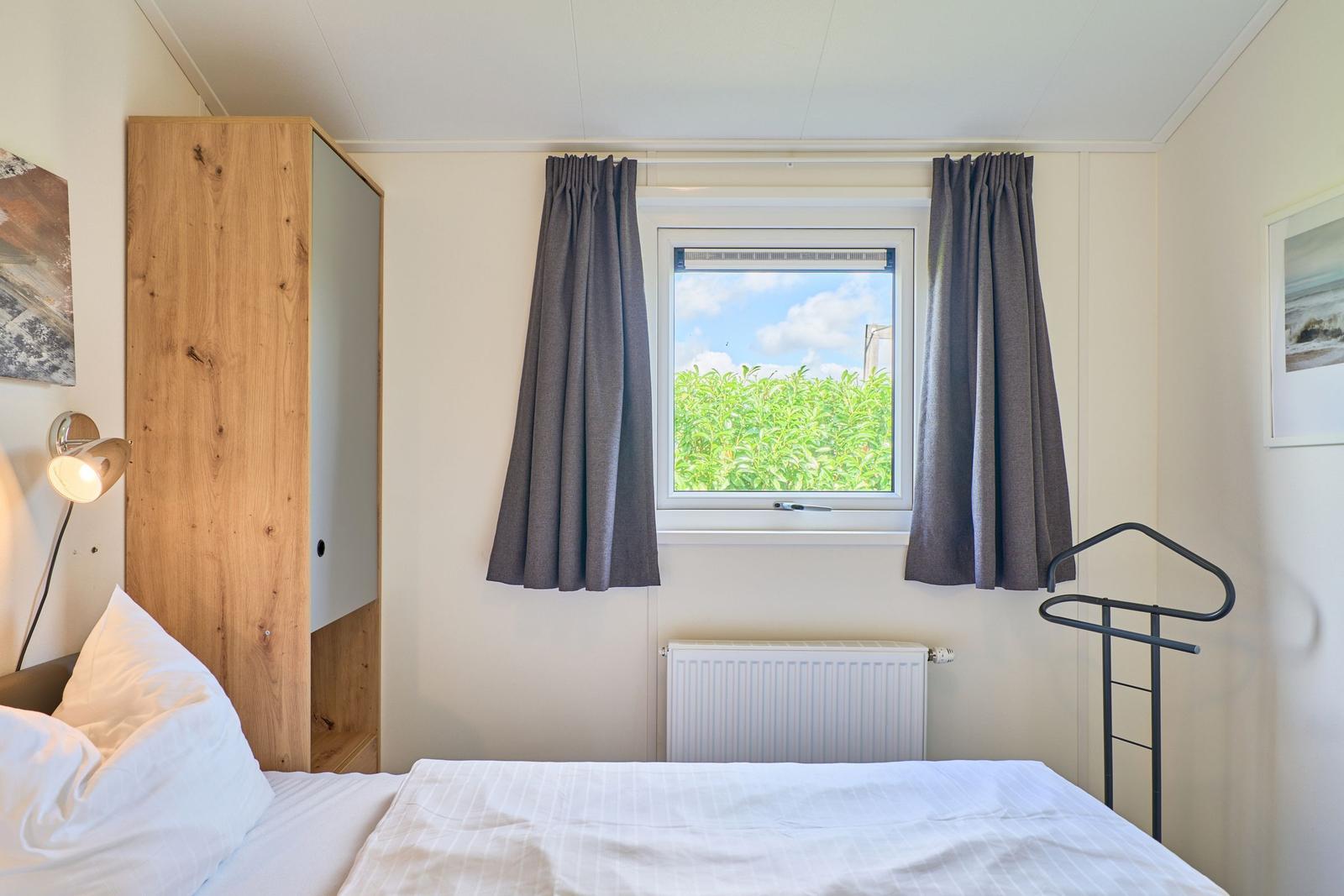 Schlafzimmer mit Bett, Fenster und Gardinen.