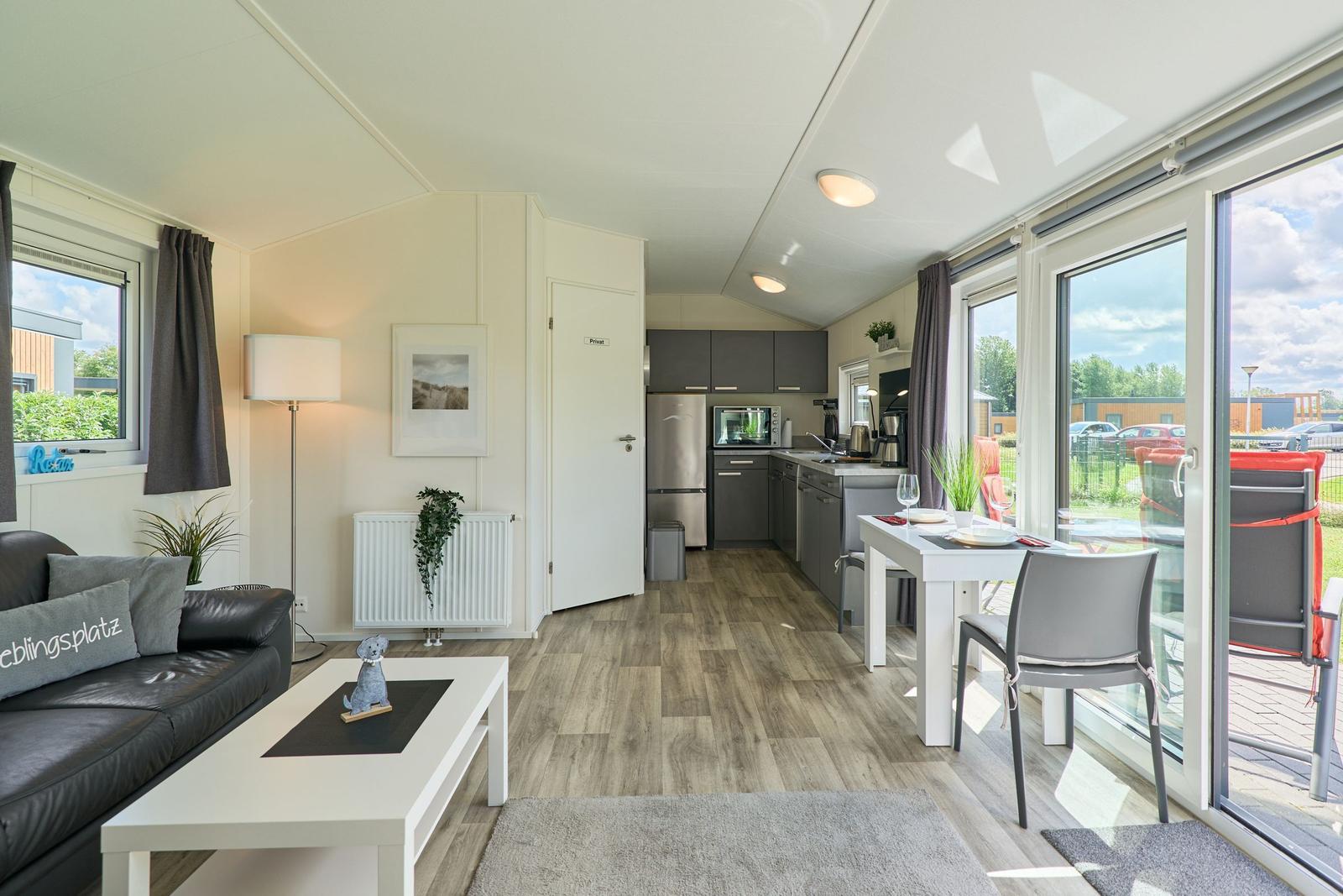 Wohnbereich mit Küche, Esstisch und Schlafzimmer. Holzboden, große Fenster und Balkon.