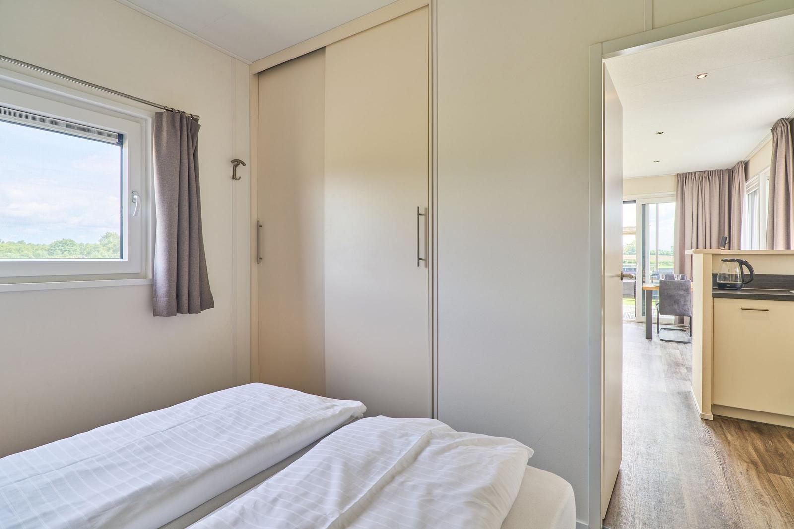 Schlafzimmer mit Doppelbett, Schrank und Fenster. Durchgang zur Küche.