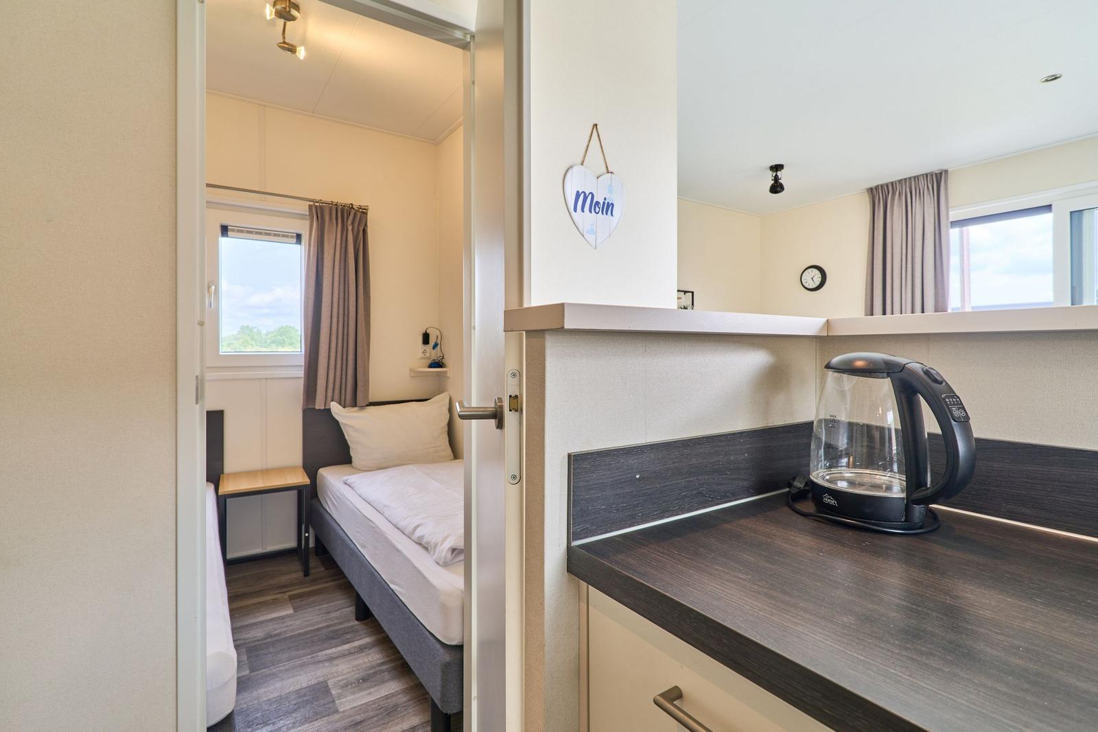Schlafzimmer mit Bett und Fenster. Küchenzeile mit Wasserkocher.