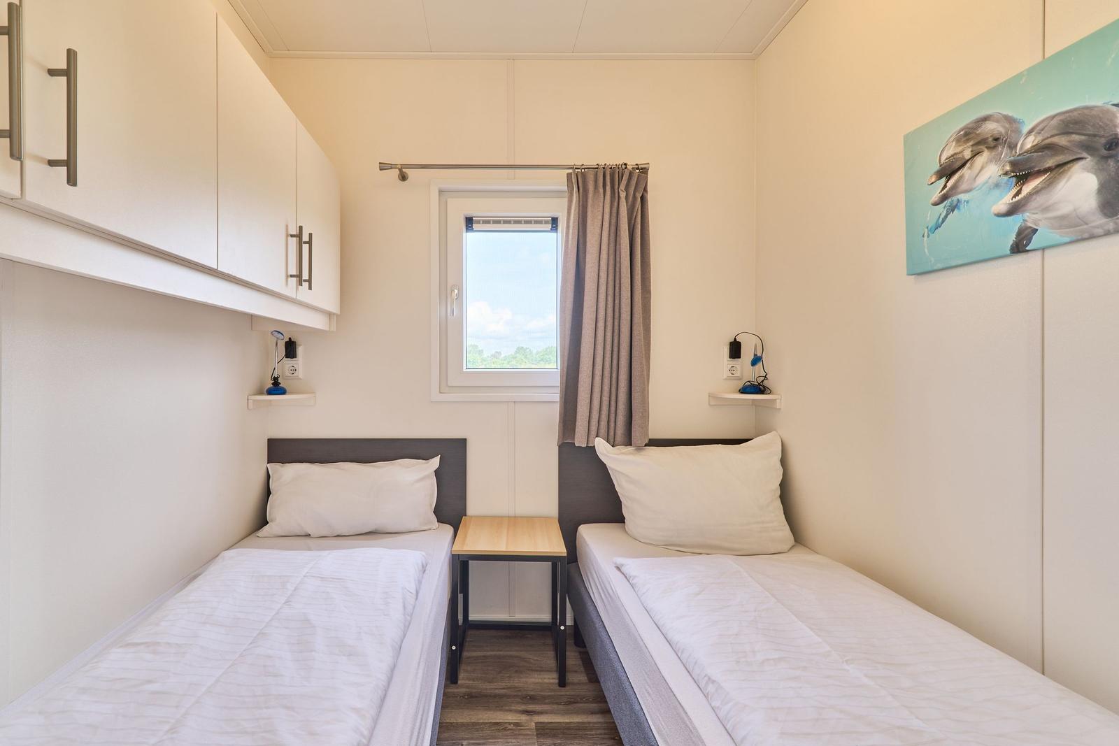 Zwei Einzelbetten mit Nachttisch und Fenster. Wandbild mit Delfinen.