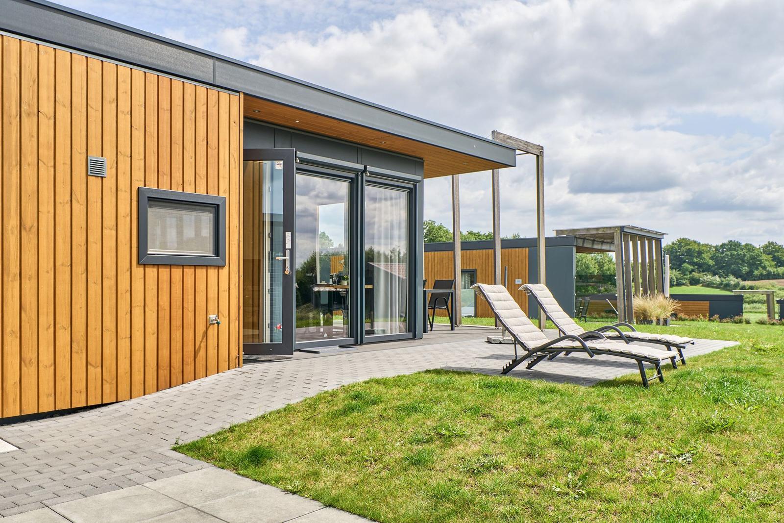 Moderne Holzhütte mit Terrasse und Liegen im Grünen.