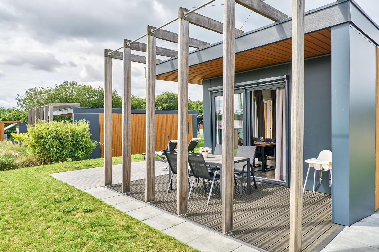 Terrasse mit Tisch, Stühlen und Hochstuhl unter Holzüberdachung.