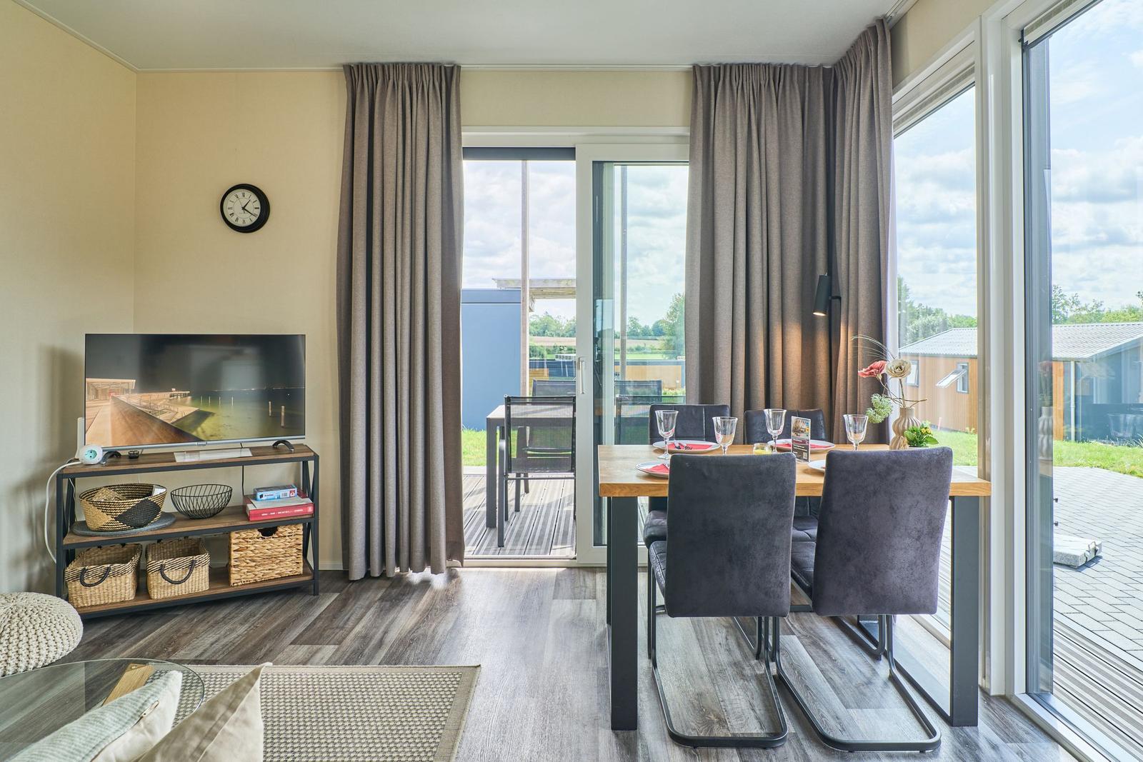 Wohn- und Essbereich mit TV, Tisch und Stühlen, großflächige Fenster zur Terrasse.