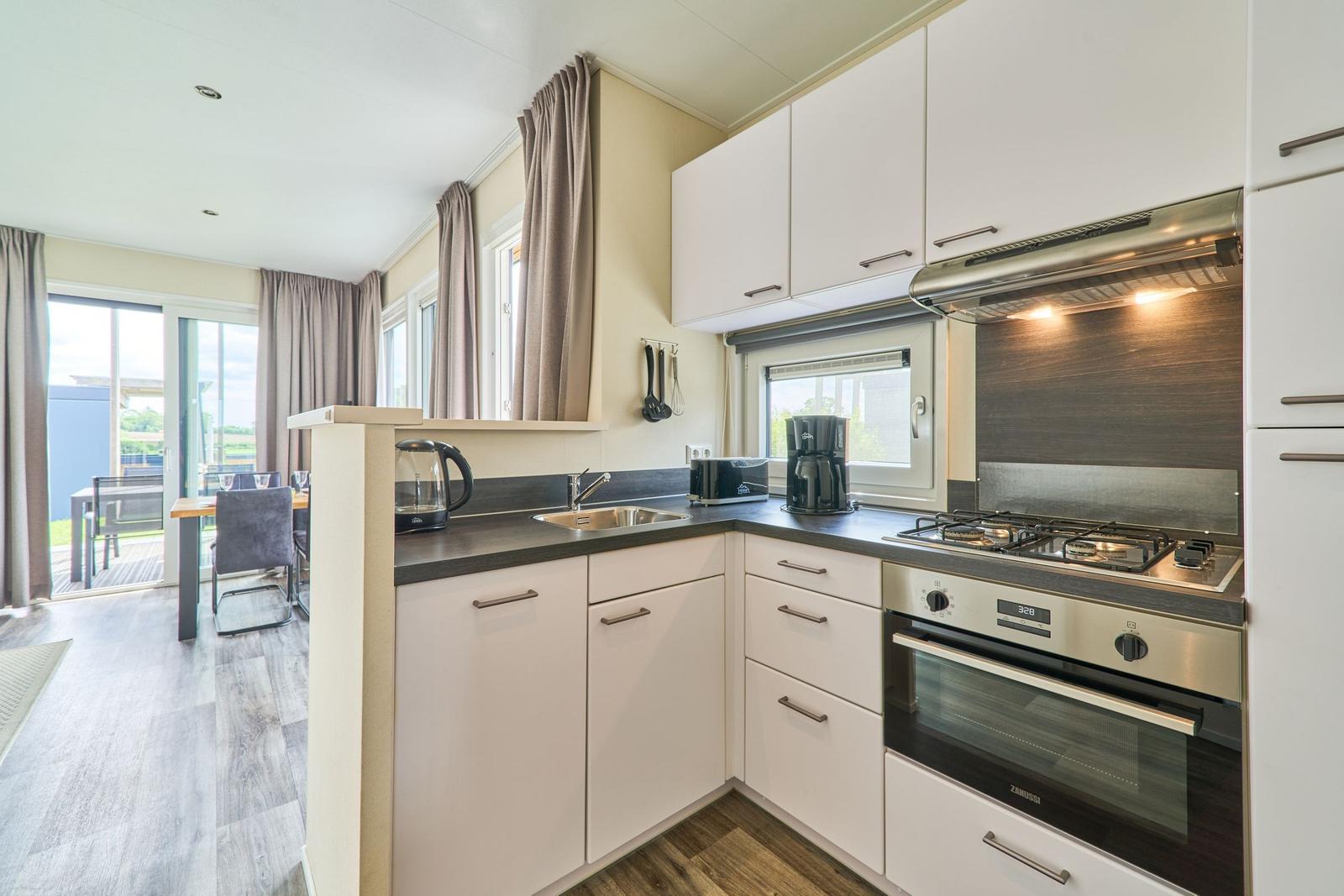 Küche mit weißen Schränken, Edelstahlherd und Blick auf Terrasse.