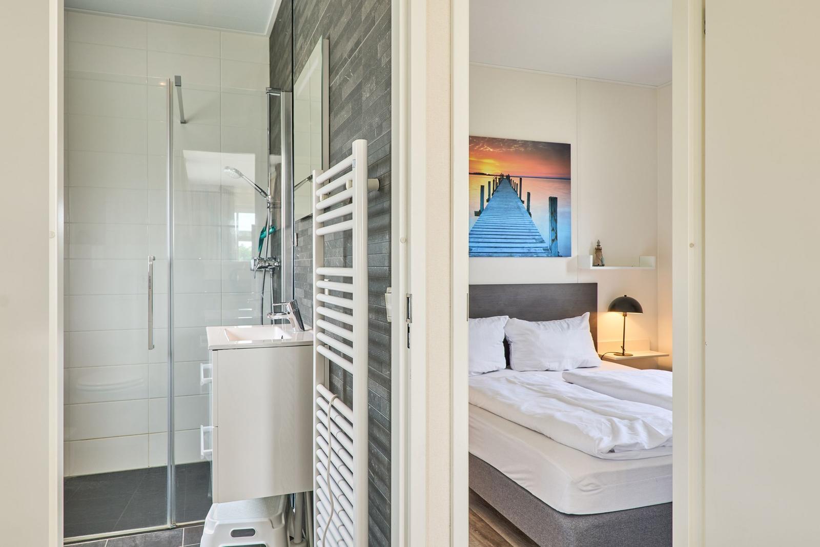 Schlafzimmer mit Bett und Wandbild. Nebenher Bad mit Dusche und Waschbecken.