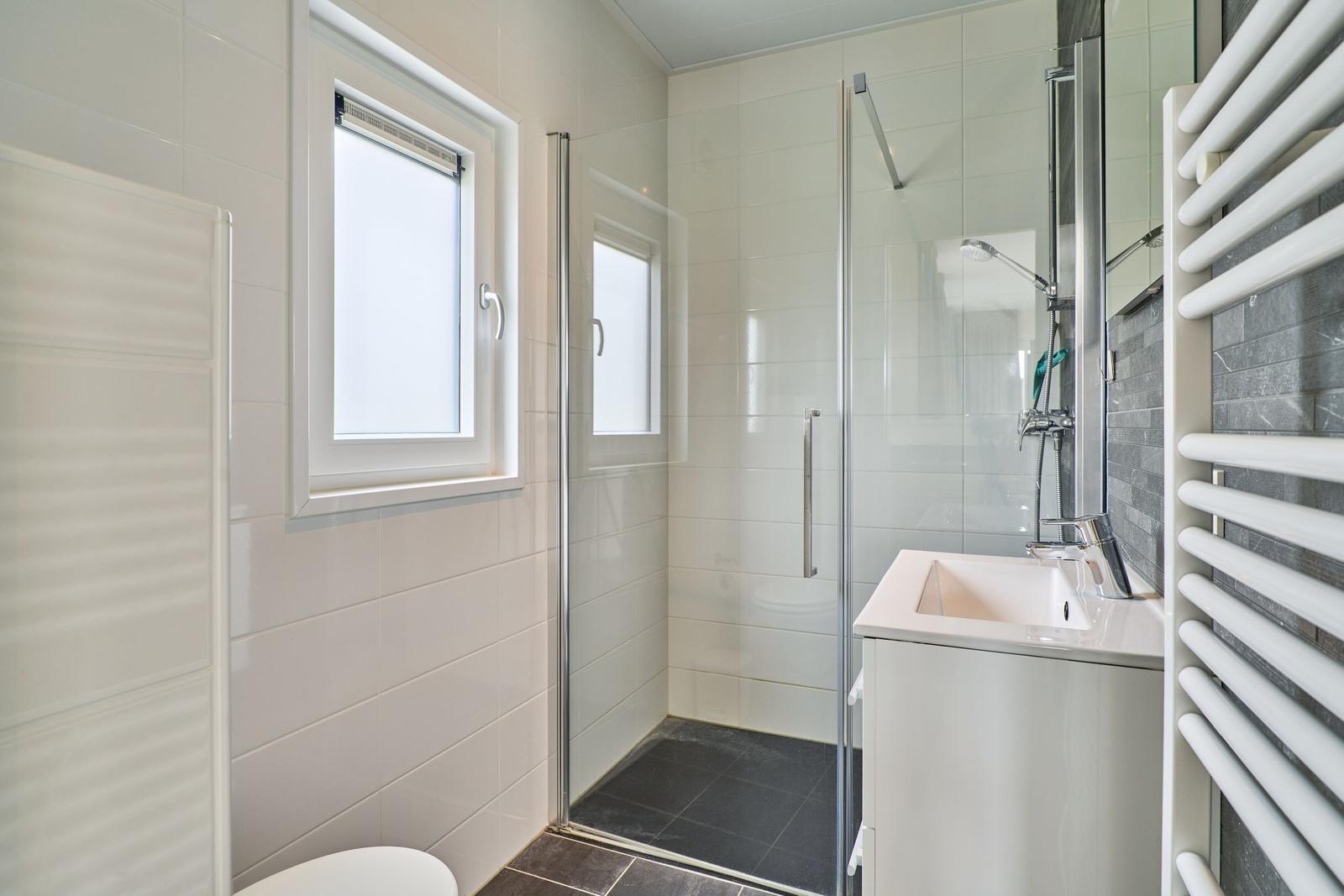 Badezimmer mit Dusche, Waschbecken und Fenster.