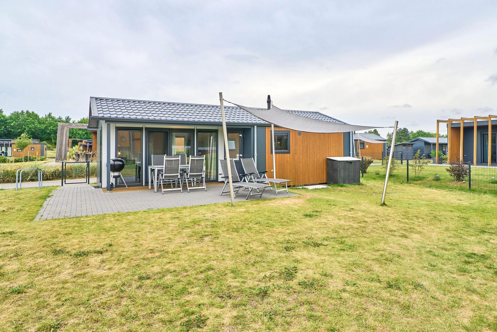 Modernes Ferienhaus mit Terrasse, Grill und Liegestühlen im Garten.
