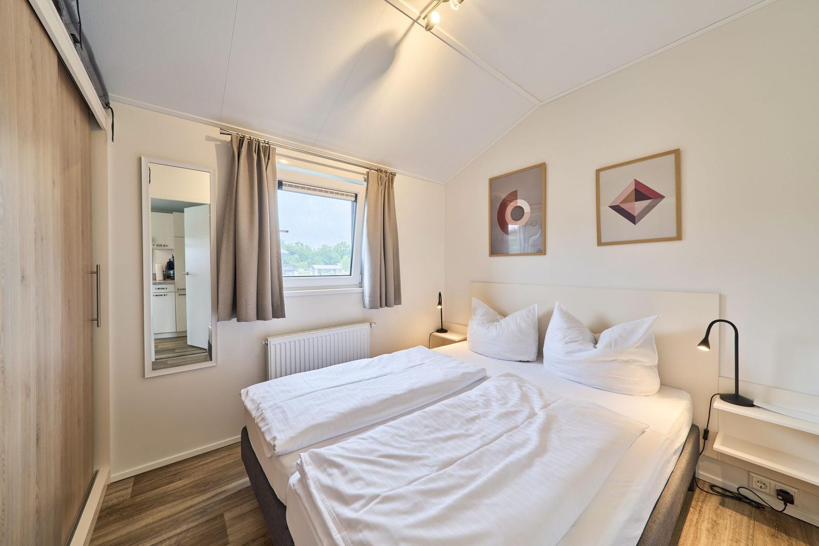 Schlafzimmer mit Doppelbett, Fenster, Spiegel und Wandbildern.