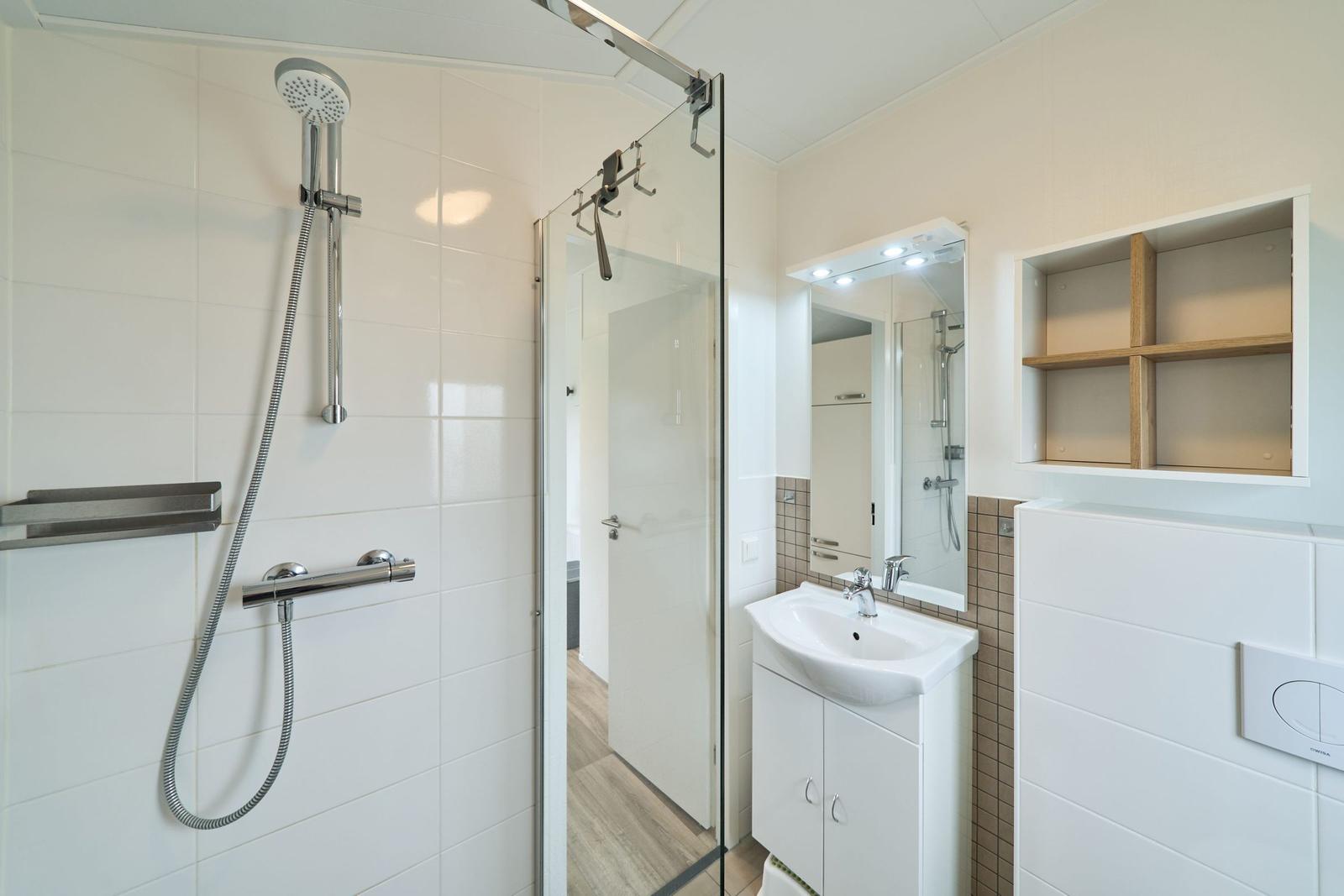 Bad mit Dusche, Waschbecken und Spiegel.