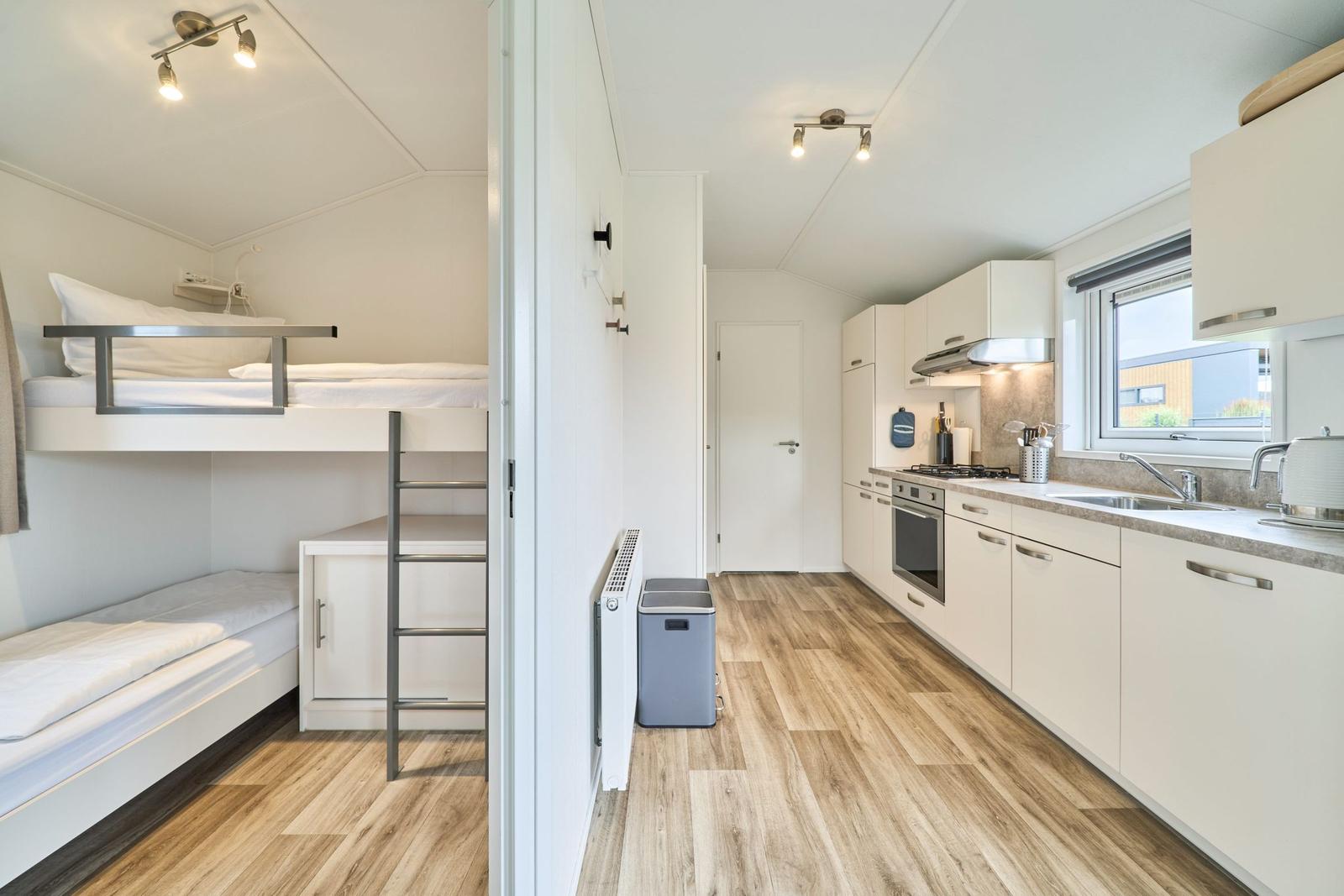 Schlafbereich mit Doppelstockbetten und Küchenbereich mit Arbeitsplatte und Fenster.