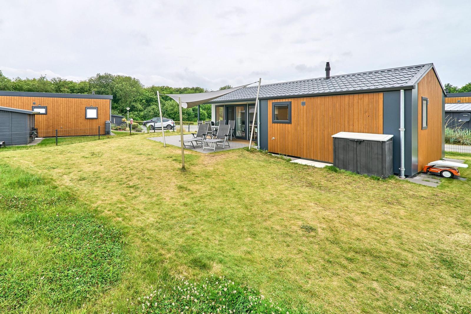 Modernes Ferienhaus mit Garten, Sitzgelegenheiten und Terrasse unter Sonnensegel.
