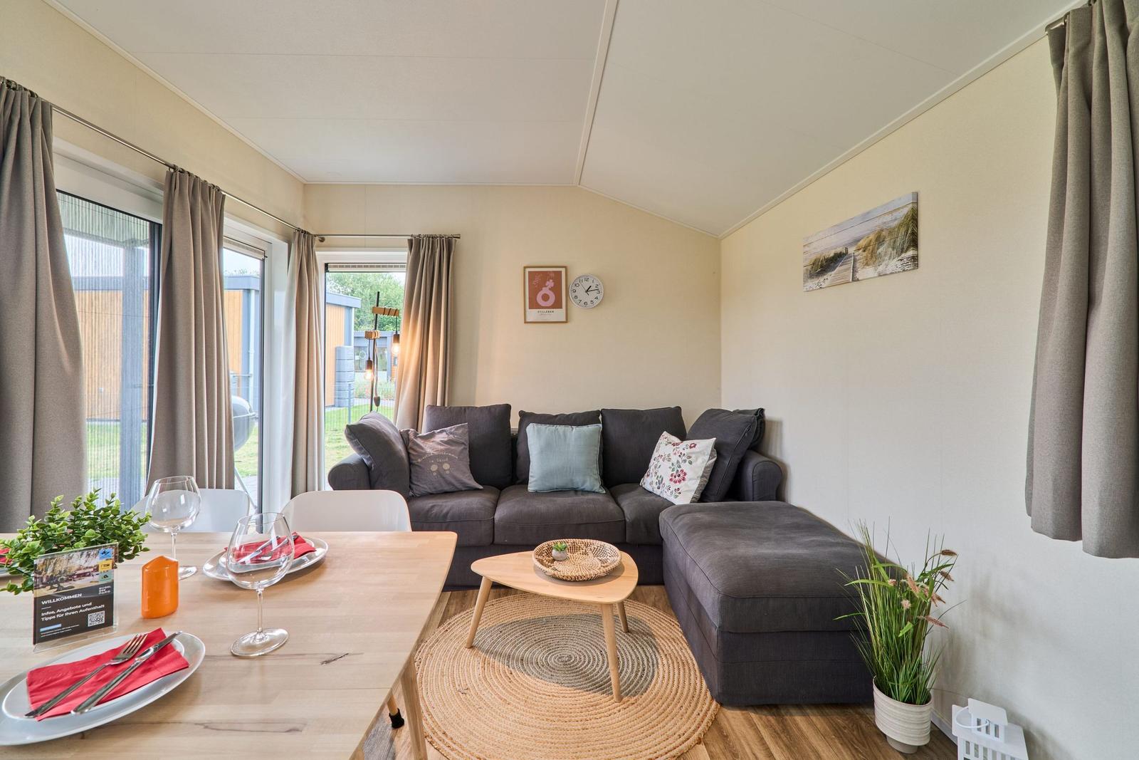 Wohn- und Essbereich mit Sofa, Tisch und Fenstern.