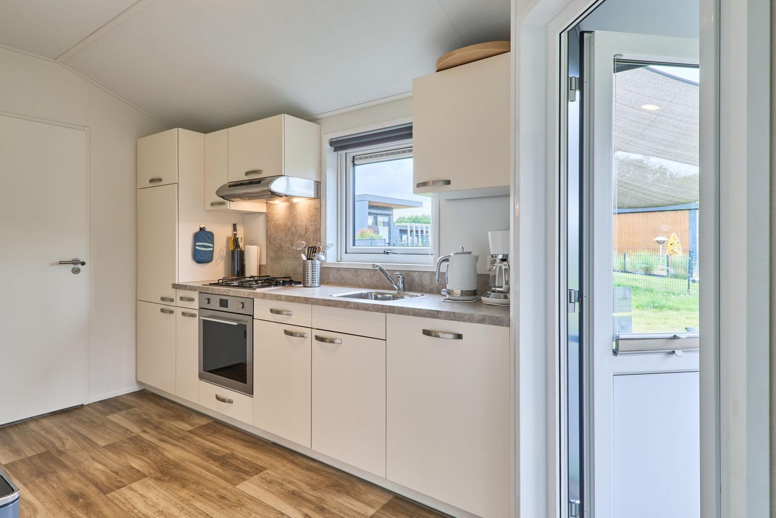 Küche mit Arbeitsplatte, Spüle, Herd und Backofen. Fenster und Tür zum Garten.